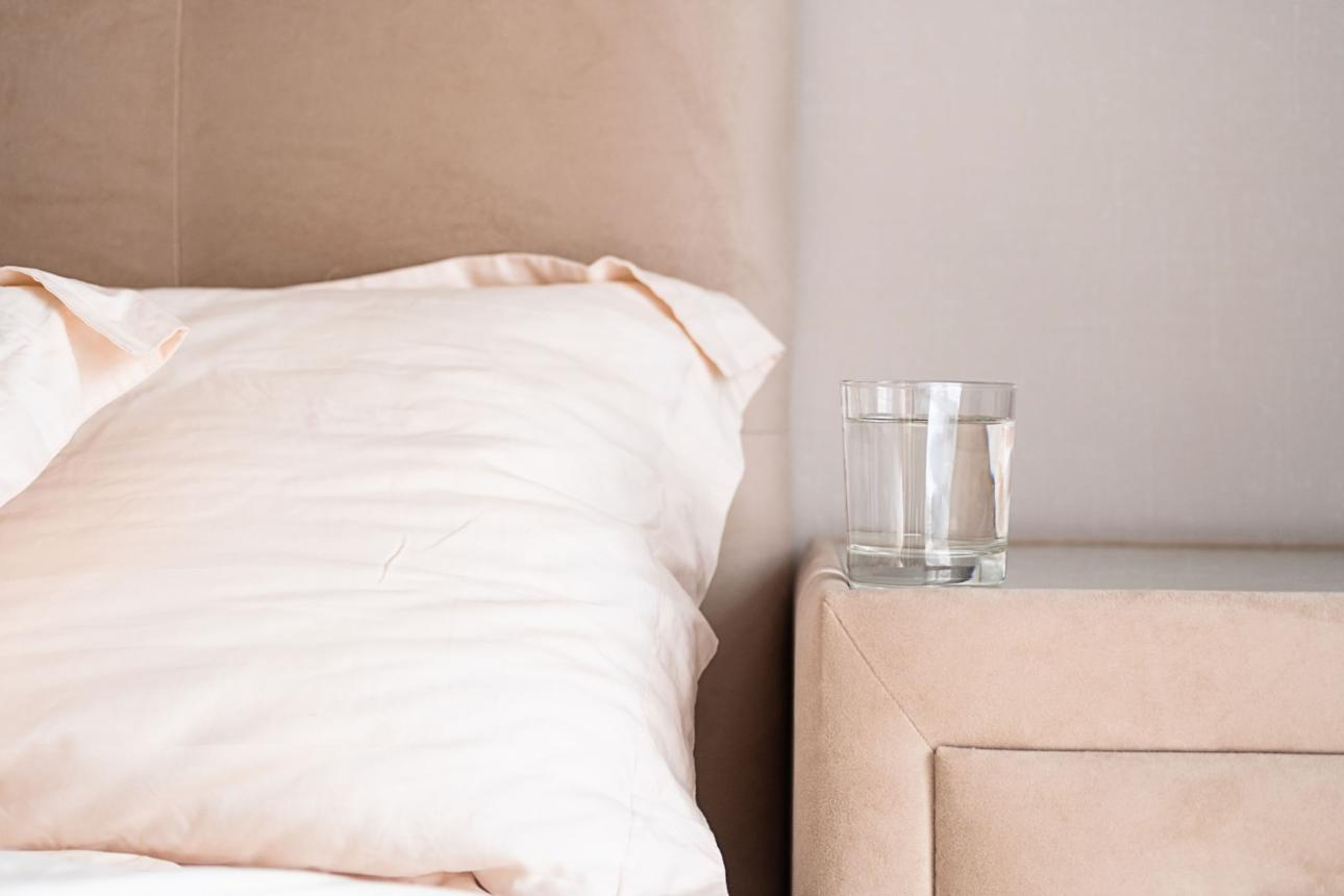 Oreiller beige sur un lit avec un verre d'eau posé sur la table de chevet — illustration des troubles urinaires nocturnes